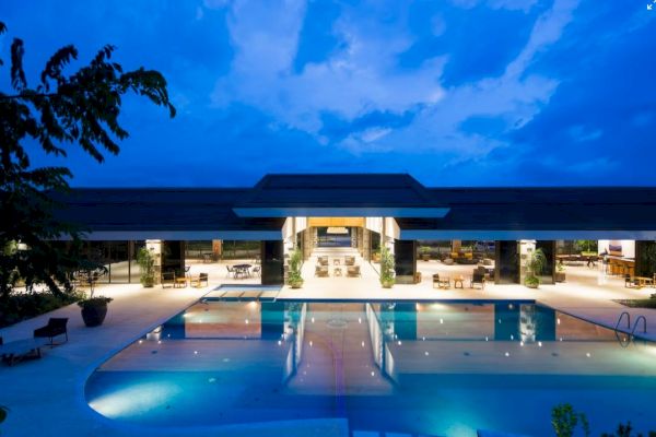 An illuminated luxury resort with a large swimming pool and surrounding lounge area against a twilight sky.