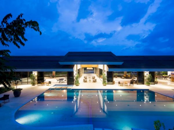 An illuminated luxury resort with a large swimming pool and surrounding lounge area against a twilight sky.