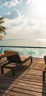 A serene poolside scene with lounge chairs, umbrellas, and a beautiful ocean view in the background, surrounded by palm trees.