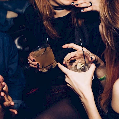 People are socializing with drinks in hand, and one person is laughing while another appears to touch their face.