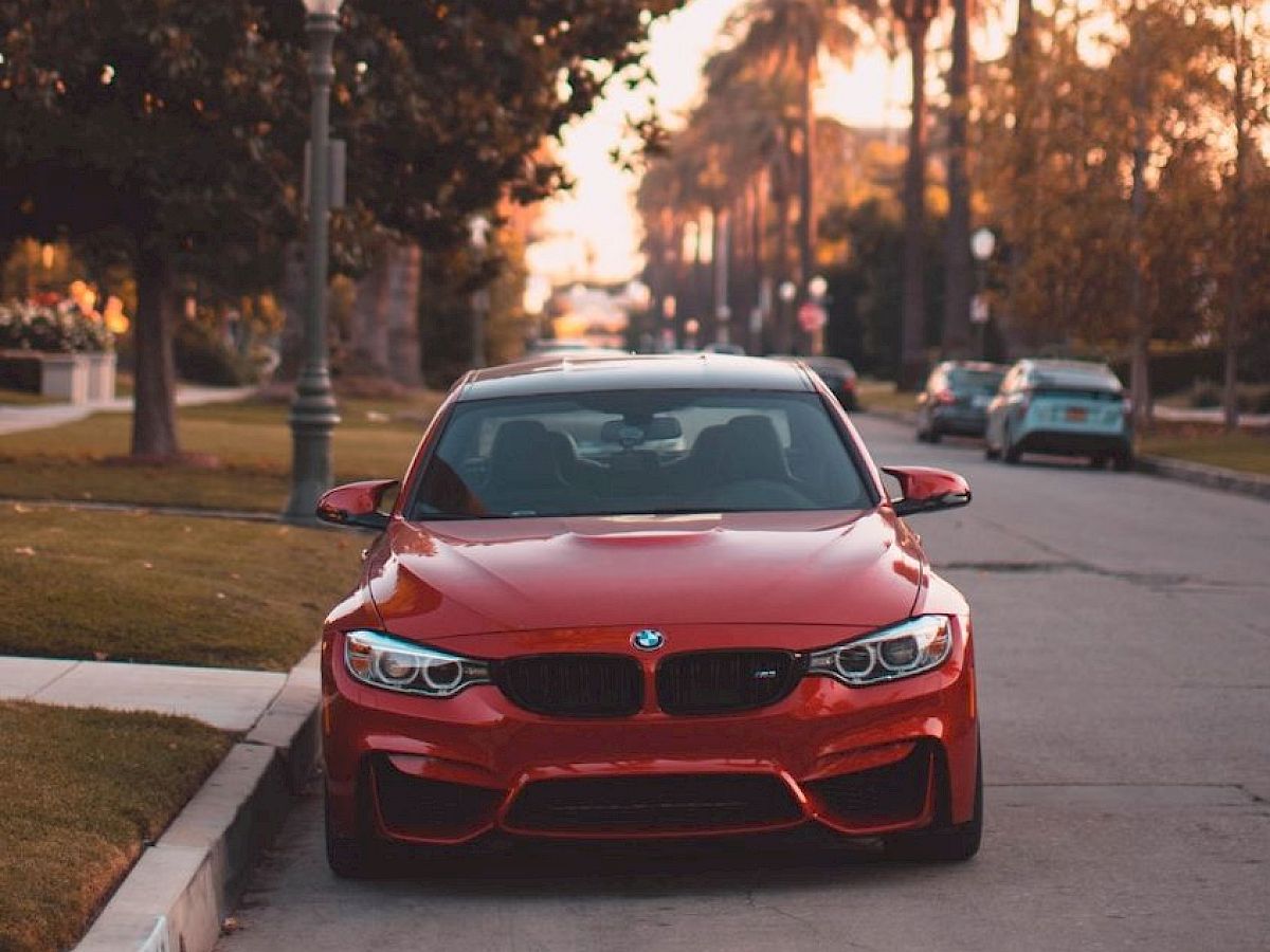 A red BMW is parked on a suburban street lined with palm trees and streetlights during either sunrise or sunset, creating a warm, serene atmosphere.