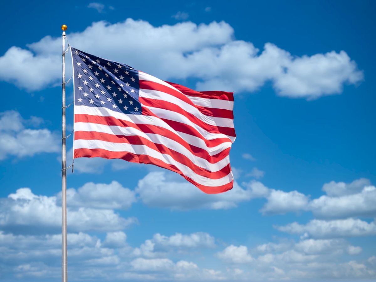 An American flag is flying against a bright blue sky with scattered clouds.