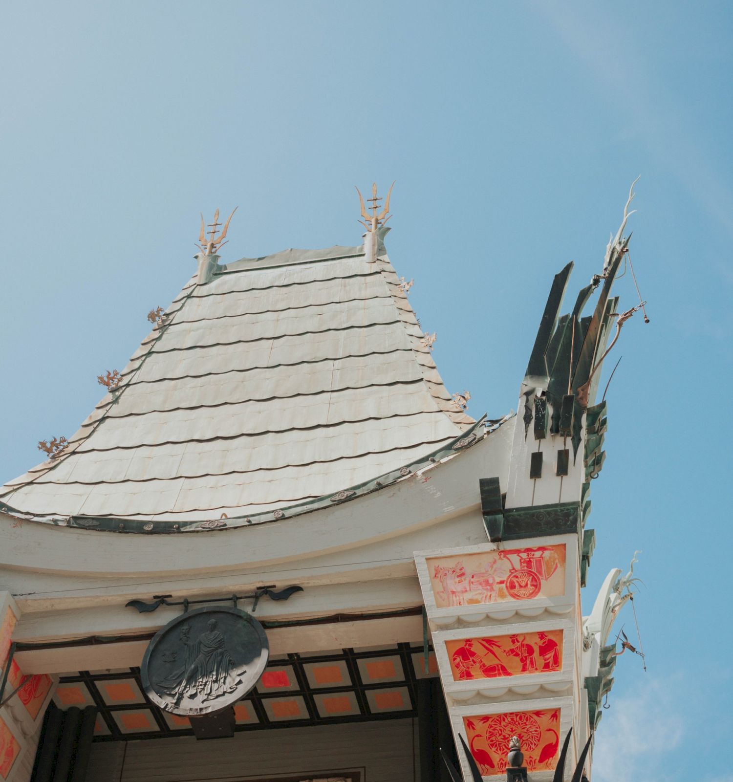 The image shows a close-up view of architectural details with an ornate roof and intricate designs, set against a bright blue sky.