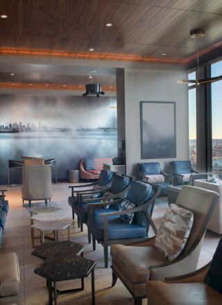 A modern lounge area with rows of comfortable chairs, large windows offering scenic views of the waterfront and a ferris wheel in the distance.