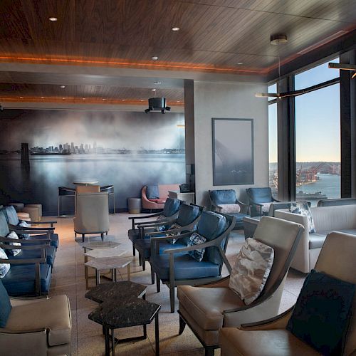 A modern lounge area with leather seating, large windows offering a scenic city and water view, and contemporary decor and lighting.