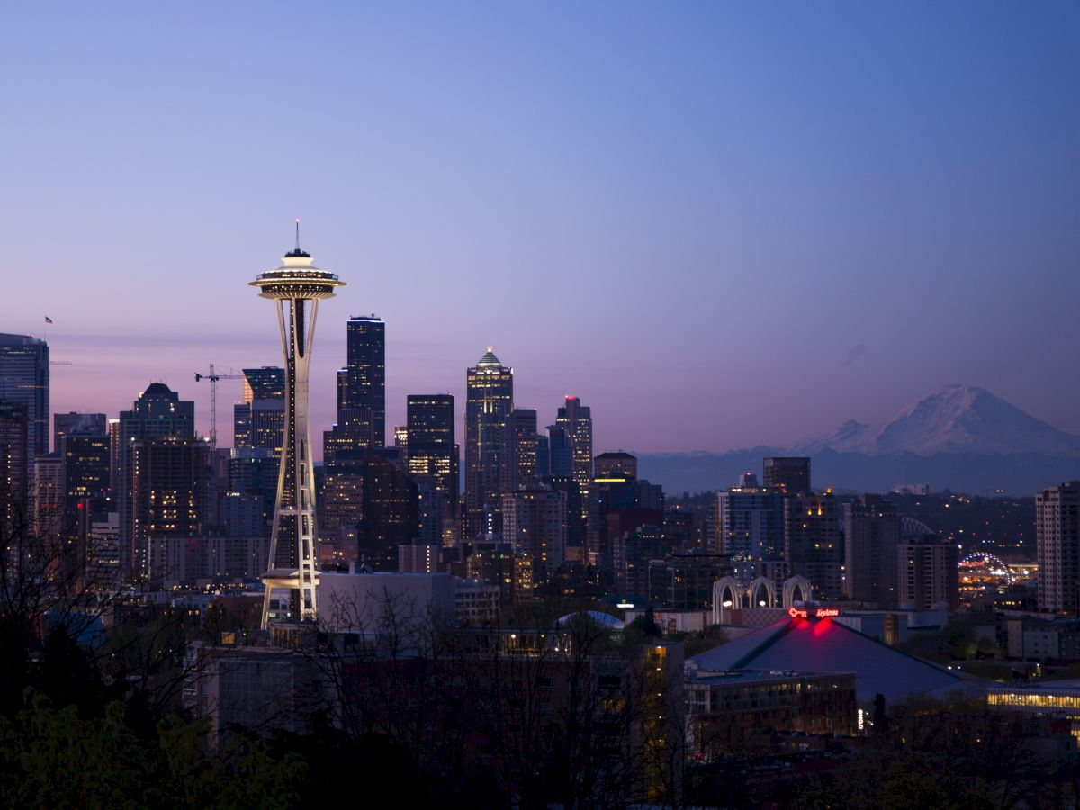 The image shows a cityscape of Seattle at dusk, featuring the Space Needle with Mount Rainier in the background.