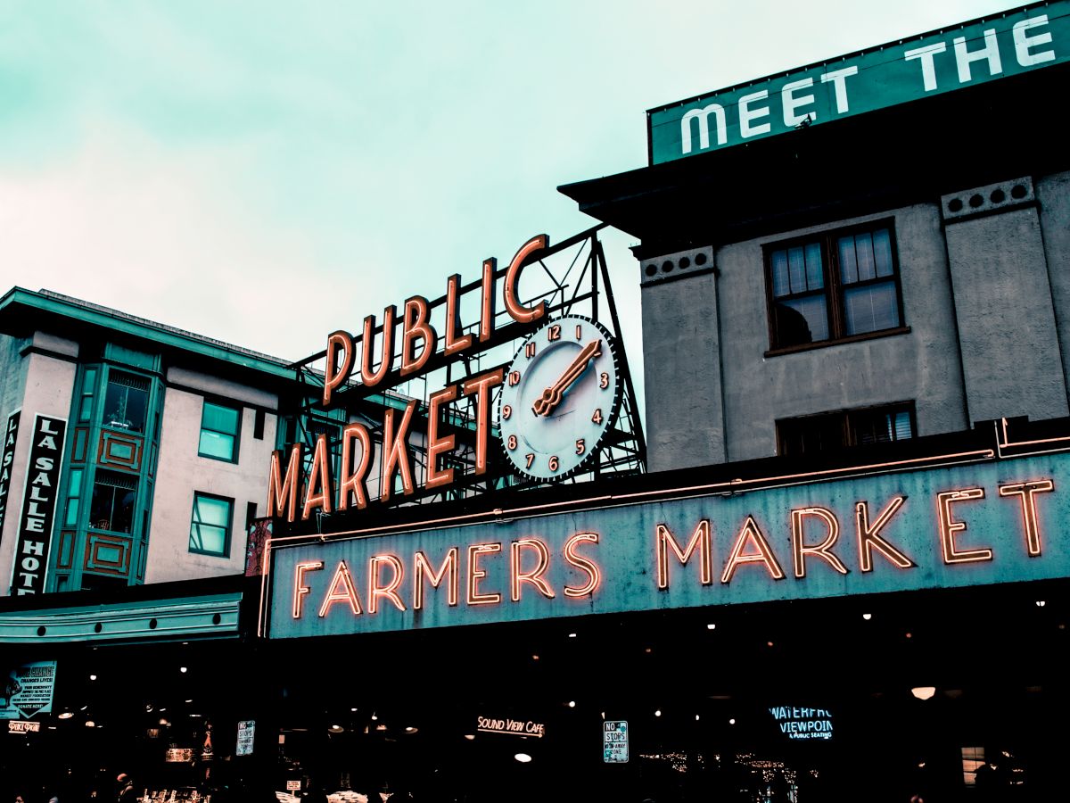 A neon sign reads "Public Market" and "Farmers Market" with buildings in the background.